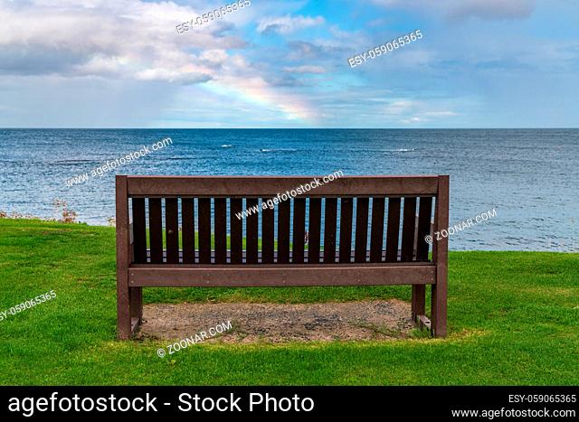A bench with a Rainbow over the North Sea coast, seen in Benthall, Northumberland, England, UK