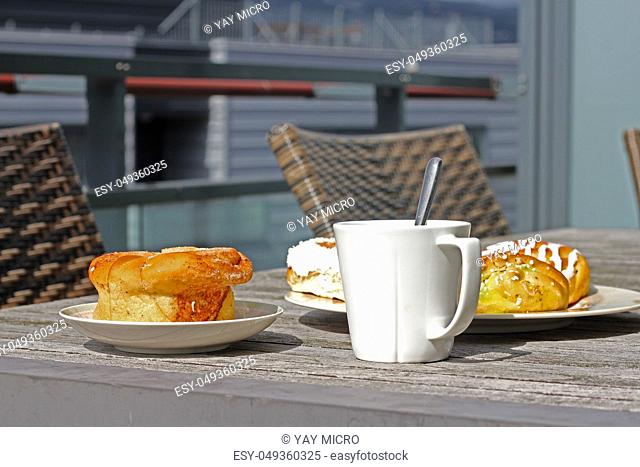 Cup of coffee and bun with cinnamon lying on outdoor wooden table in cafe