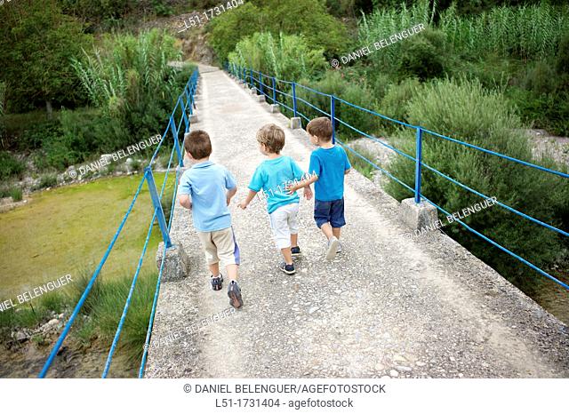 three boys crossing an old bridge on the country, Ludiente, Castellón, Spain