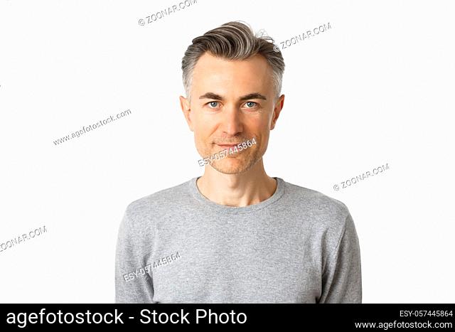 Close-up of confident, handsome middle-aged man with short gray hairstyle, smiling and looking determined, standing over white background