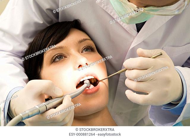 Image of young woman keeping her mouth open while dentist examining it