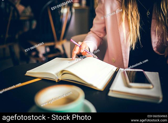 Business, education concept. Woman working in outdoor at coffee shop. Close up caucasian woman hand on wooden table inside cafe makes notes in notebook