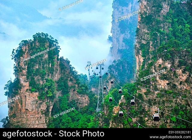 Famous tourist attraction of China - Zhangjiajie stone pillars cliff mountains in fog clouds with cable railway car lift at Wulingyuan, Hunan, China