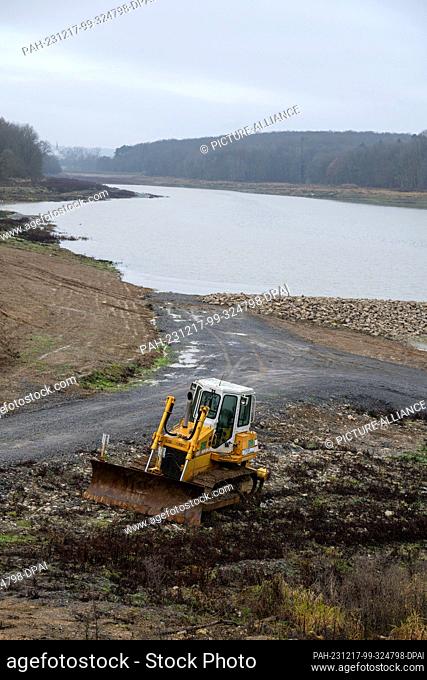 PRODUCTION - 15 December 2023, Bavaria, Stadtlauringen: An excavator stands at the edge of Lake Ellertshausen, behind it a new dam stretches through the main...