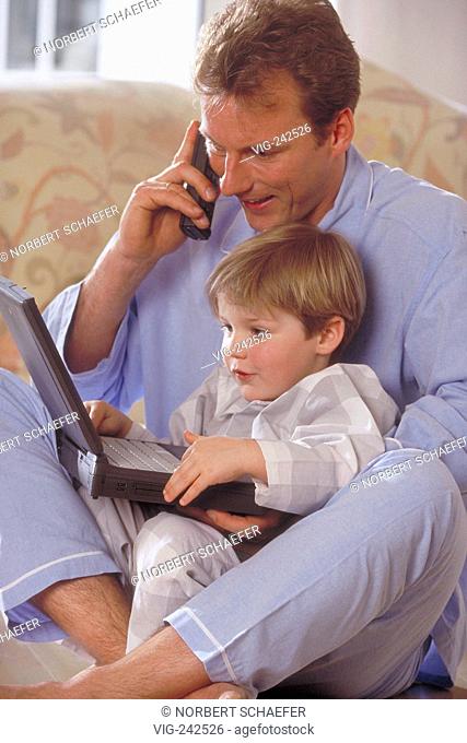 indoor, man sits with his son and a notebook on his knees on a sofa making a call with the mobile phone  - GERMANY, 26/02/2005