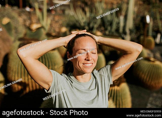 Happy woman with hands behind head in cactus garden