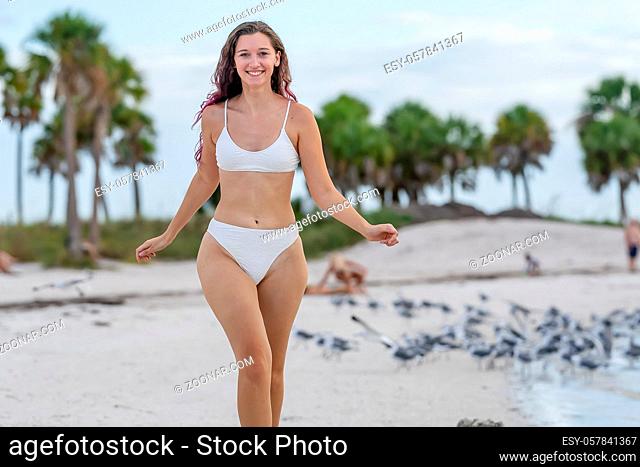 A beautiful brunette bikini model enjoys the weather outdoors on the beach while chasing seagulls