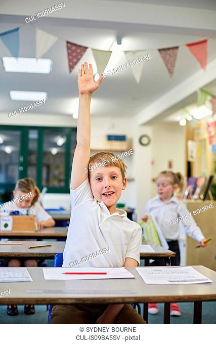 Schoolboy with hand up in classroom at primary school
