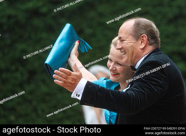 25 July 2023, Bavaria, Bayreuth: Presenter Wolfram Kons and wife Alexa Apermann arrive in the rain for the opening of the Richard Wagner Festival with a new...
