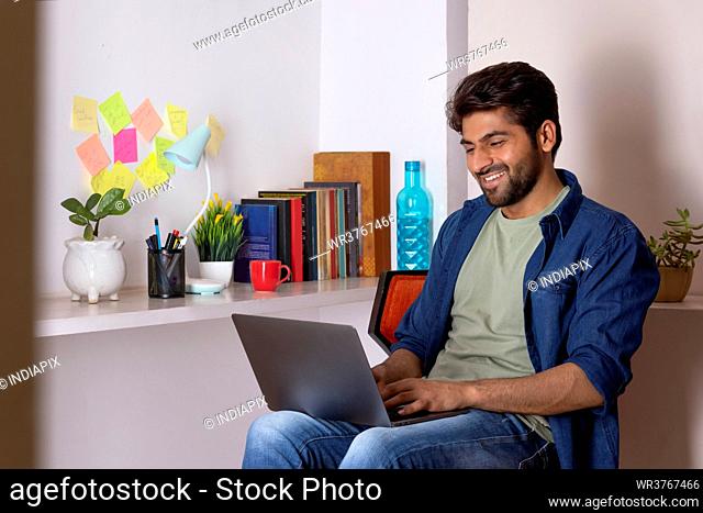 A HAPPY YOUNG MAN CHEERFULLY WORKING AT OFFICE