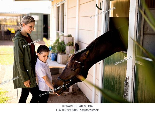 Mother and daughter feeding a horse in the stable