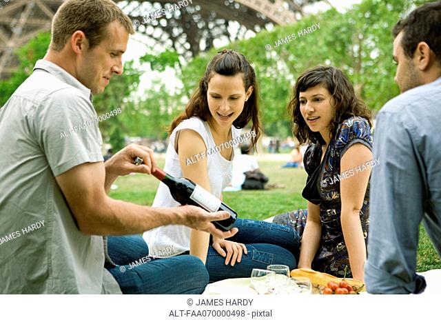 Friends enjoying picnic outdoors, admiring bottle of wine