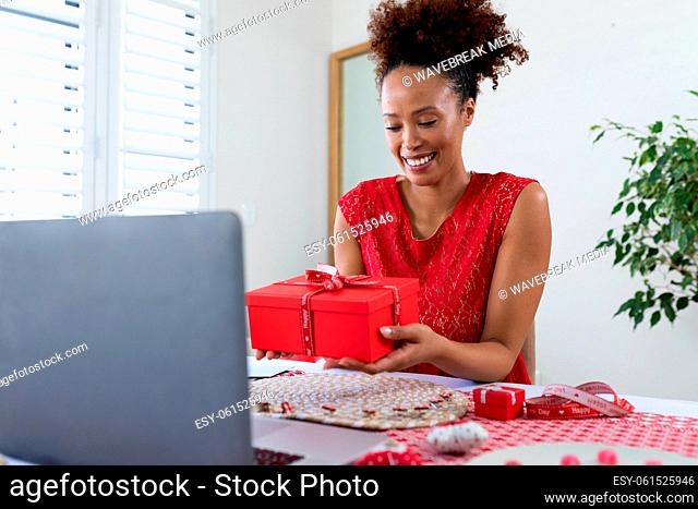African american woman holding gift box on videocall on laptop at home