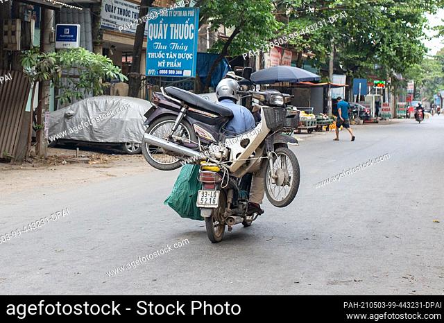 23 April 2021, Vietnam, Hanoi: A rider transports a broken motorcycle on the luggage rack of his bike to Te Lo village.