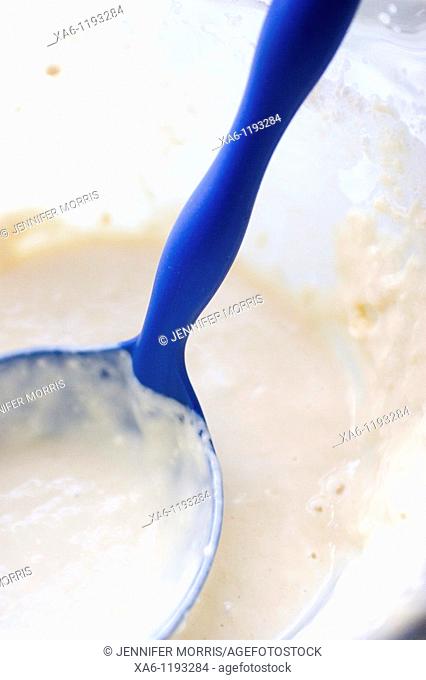 A blue plastic ladle rests in a bowl of pancake batter