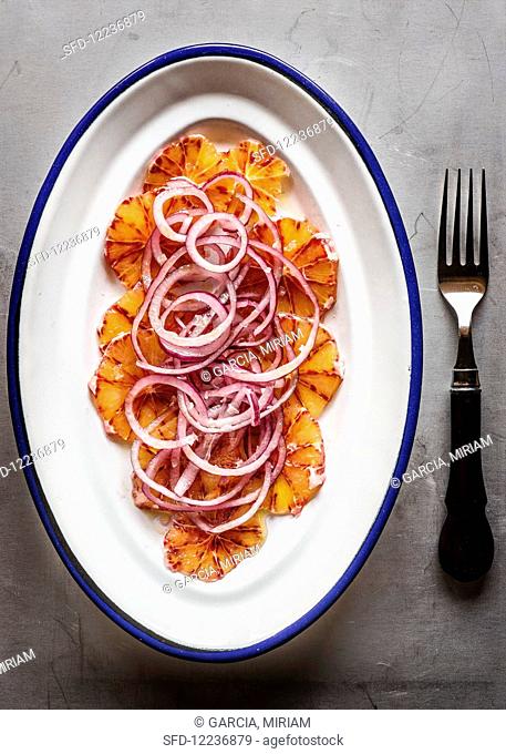 Salad with sliced blood orange and red onion on white-blue platter, metal background