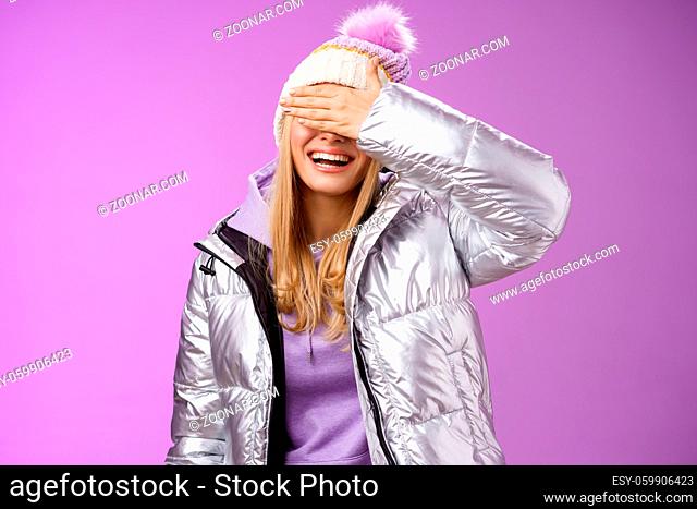 Happy relaxed smiling attractive young blond woman in stylish warm silver jacket hat hide eyes behind palm laughing happily waiting boyfriend prepared surprise...