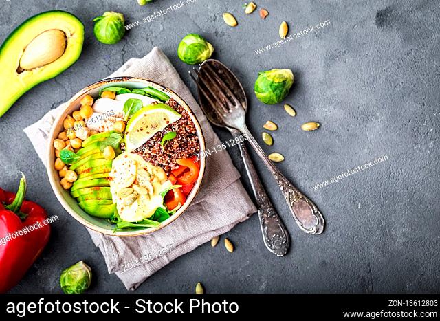 Bowl with healthy salad on grey concrete background. Space for text. Bowl with mix of chickpea, avocado, chicken, quinoa seeds, red bell pepper, fresh spinach