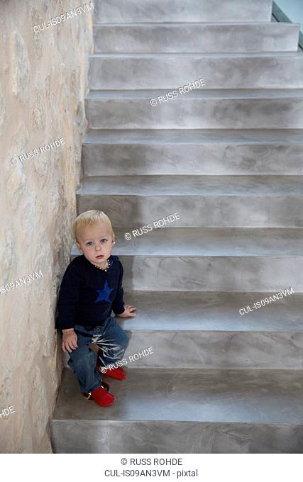 Portrait of male toddler sitting on house staircase
