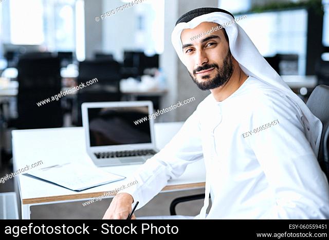 Handsome man with dish dasha working in his business office of Dubai. Portraits of a successful businessman in traditional emirates white dress
