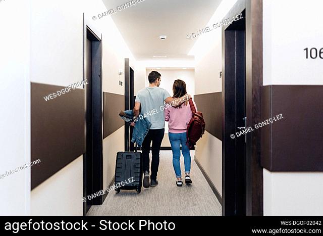 Couple walking with luggage at hotel corridor