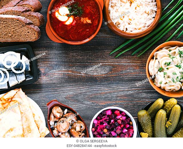 Russian food on wooden background. Assortment dishes of Russian cuisine - borscht, pelmeni, herring, marinated mushrooms, salted cucumbers, vinaigrette
