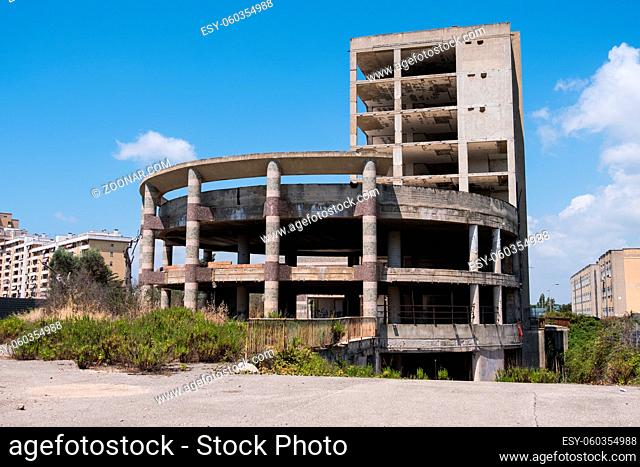 Huge multi floors concrete structure of abandoned building with stairs surrounded by grass and trees with blue sky in the background