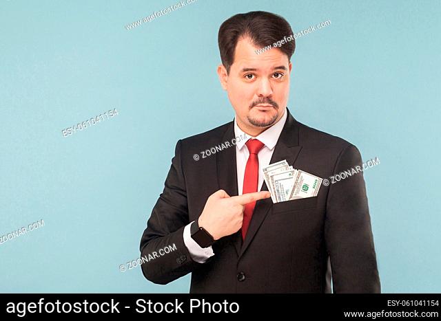 Businessman pointing finger at money in the pocket of a bribe. Indoor, studio shot, isolated on light blue or gray background