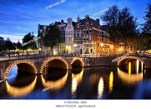 Night scene at a canal with traditional buildings and an arch bridge in Amsterdam, Netherlands