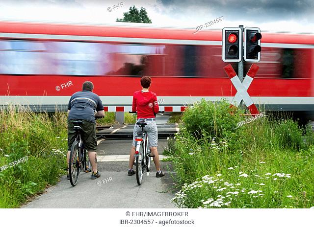 A man and a woman with bicycles standing at a closed railway crossing, Grevenbroich, North Rhine-Westphalia, Germany, Europe