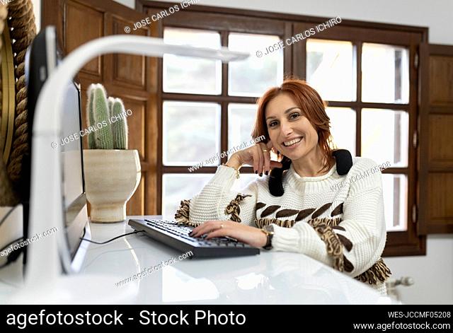 Happy businesswoman sitting by computer keyboard in home office