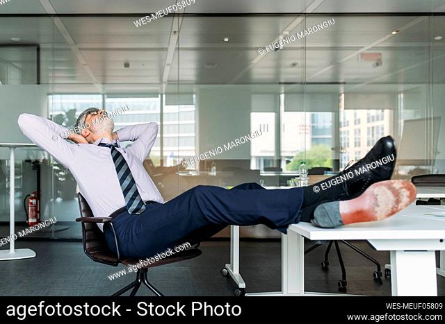 Mature businessman with hands behind head relaxing on chair in office