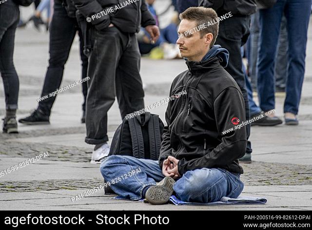 16 May 2020, Hamburg: A participant of a meditation demonstration at the Hamburg town hall market sits in lotus position on the stones