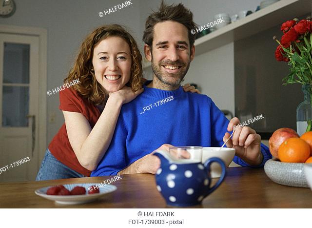 Portrait of smiling mid adult couple at table with breakfast in room