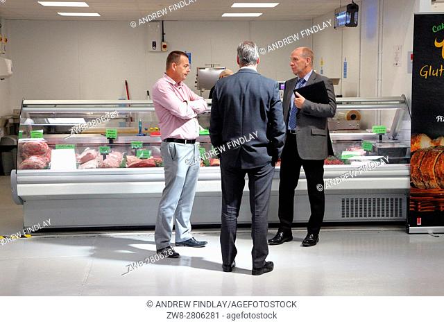 Three men chatting in front of Butchery section of a food wholesaler
