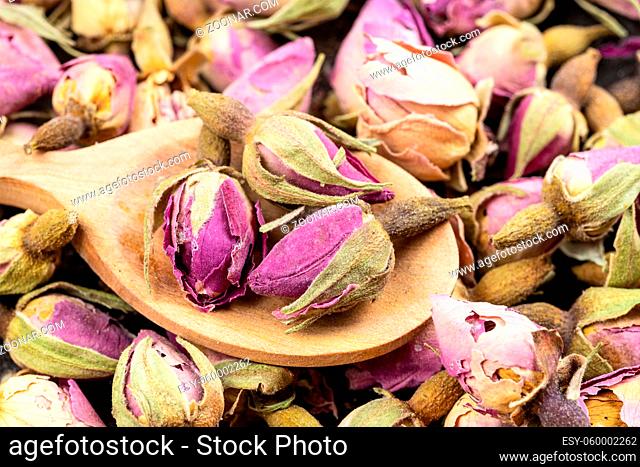 old dried rosebuds close up in wood spoon on pile of dried flowers