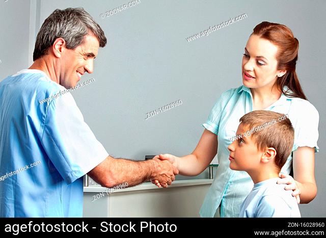 Frau mit Kind schüttelt einem lächelnden Arzt die Hand