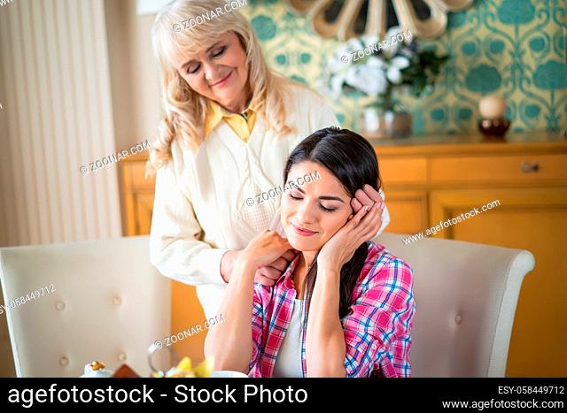 Charming Daughter Sits With Her Eyes Closed While Her Elderly Mother Gently Hugs Her Head. Tenderness. Family Concept