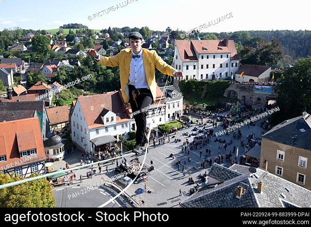 dpatop - 24 September 2022, Saxony, Hohenstein: The slackline runner Ruben Langer runs on a rope between the castle and the town church across the market square...