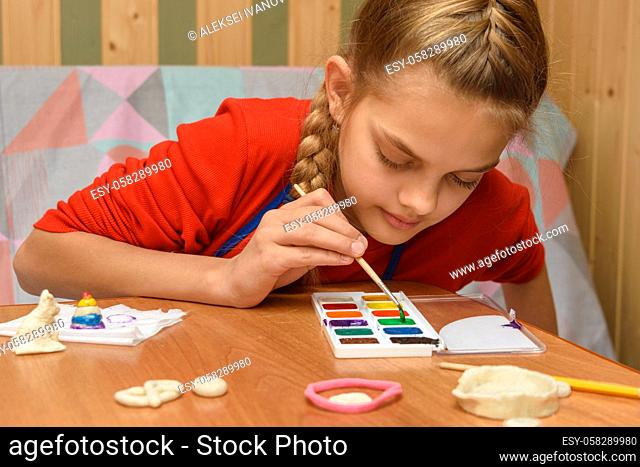 A girl chooses a color of watercolors for coloring dough figurines