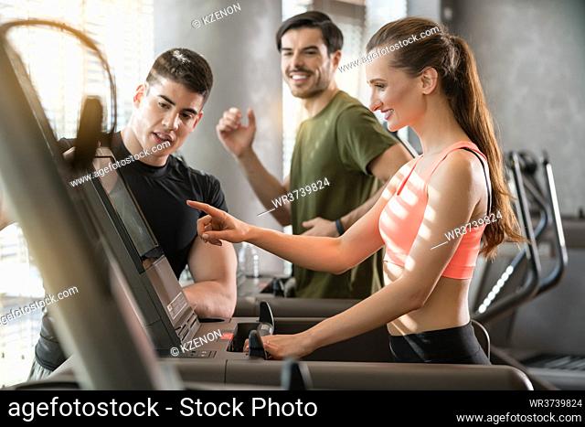 Motivated young woman increasing the speed of the treadmill during a workout session supervised by a professional personal trainer