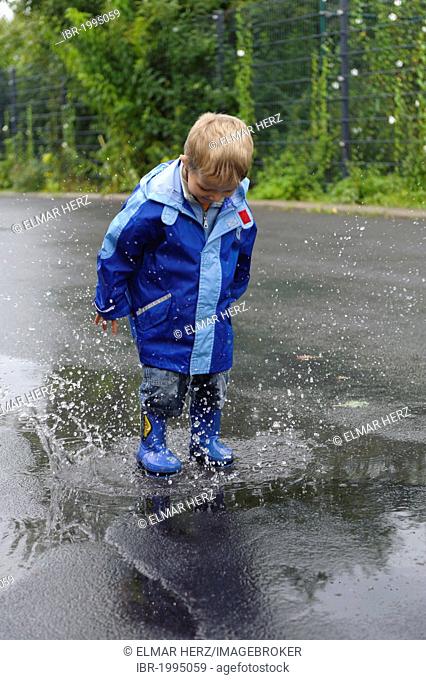 4-year-old boy jumping in a puddle on the road in the rain, Assamstadt, Baden-Wuerttemberg, Germany, Europe