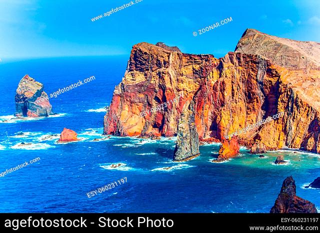 The west coast of the island of Madeira - red rocks, turquoise surf. The blinding midday sun illuminates the rocky shore