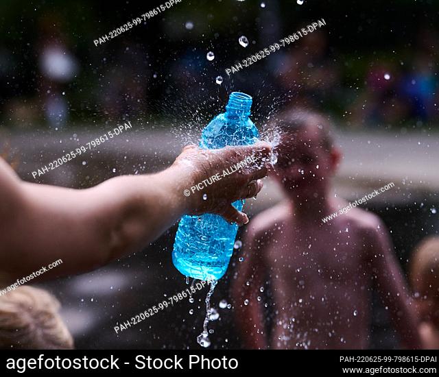 25 June 2022, Berlin: A mother fills water from the fountain for her son. The heat is sweltering in Berlin this weekend. Photo: Annette Riedl/dpa