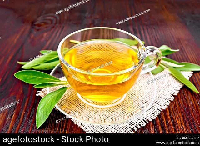 Herbal tea with sage in a glass cup on a burlap napkin on a wooden board background