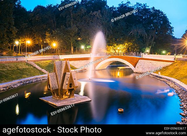Gomel, Homiel, Belarus. Scenic View Of Park Watercourse Channel Flowing Into River Through Stone Bridge In City Park In Evening Or Night Illumination