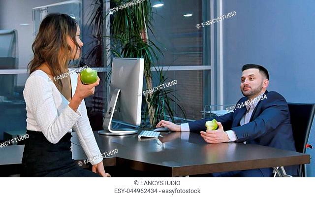 Two office workers having a break, aeting green apples and talking in office. Professional shot in 4K resolution. 085. You can use it e.g