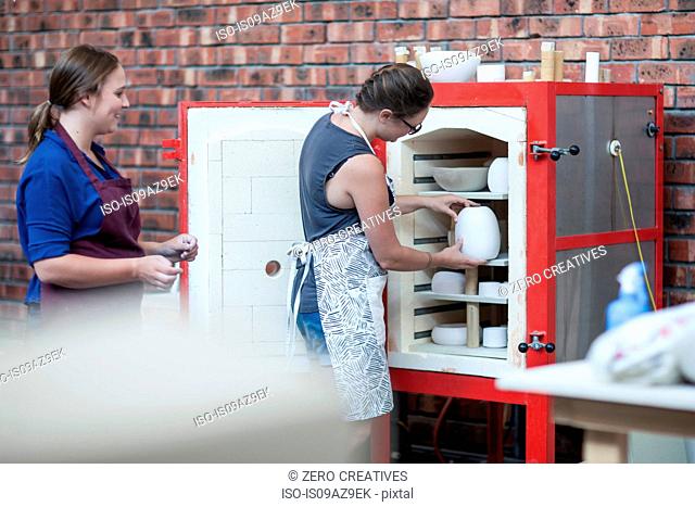 Female potter putting vase into workshop kiln