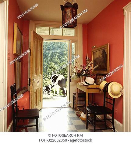Straw hats on antique chairs in red hall with blue+white checked floor and open door with view of model cows
