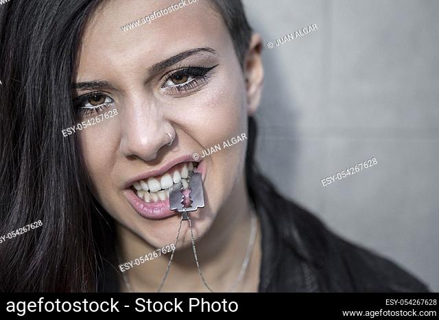 Attractive woman holding razor necklace in mouth and looking at camera